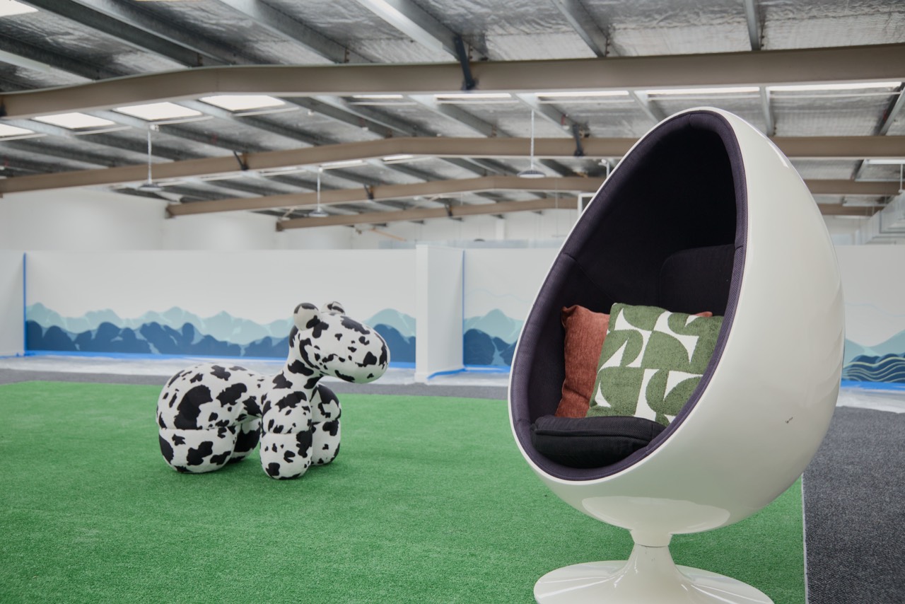 A white egg chair and a cow-print seat on the artificial grass